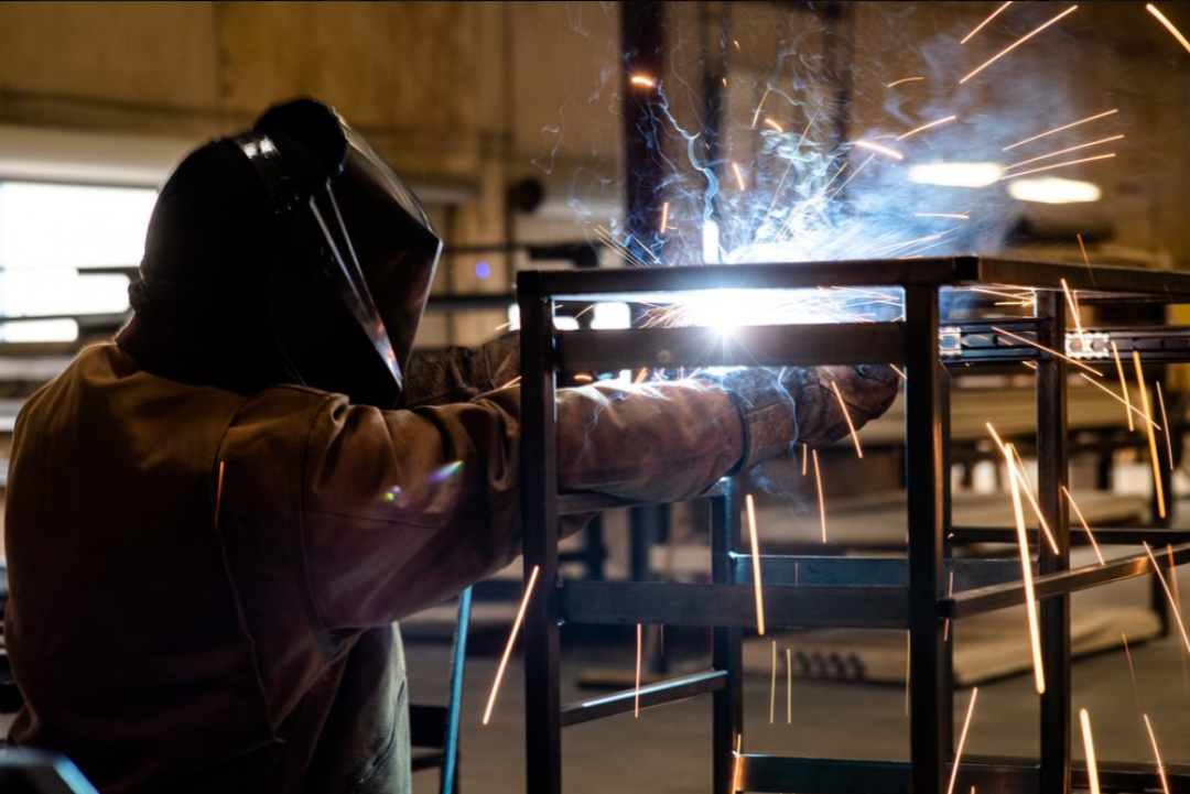 Welder with protective helmet fabricating steel frame, industrial photography Dallas, Texas