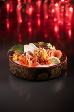Sashimi platter with uni and edible flowers in ornate Japanese bowl, food photography Dallas, Texas