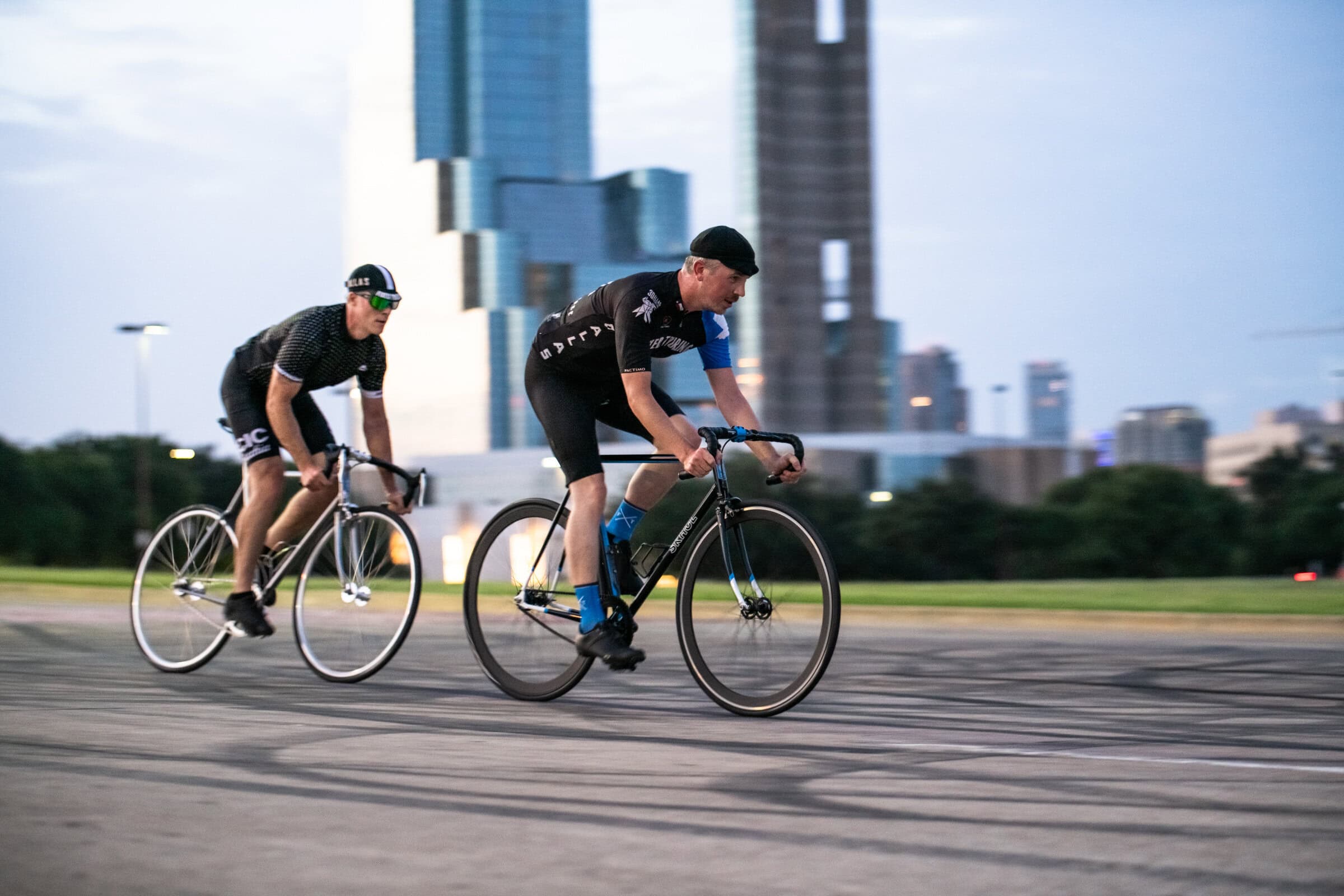 Two cyclists racing on SKHUL Bicycles fixed-gear bikes with Dallas skyline, commercial photography Dallas, Texas