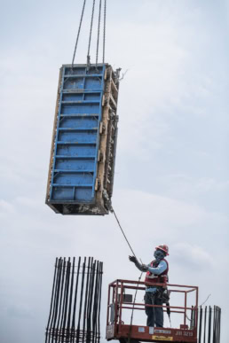 TAS Concrete worker guiding crane-lifted formwork on construction site, industrial photography Houston, Texas