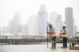 TAS Concrete workers using Topcon surveying equipment on construction site with Houston, Texas skyline