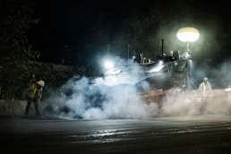 Topcon asphalt paver laying road at night with steam and balloon light, industrial photography Fort Worth, Texas