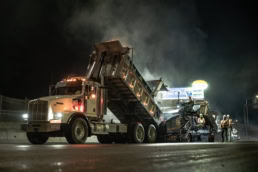 Topcon nighttime asphalt paving operation with dump truck and paver, industrial photography Fort Worth, Texas