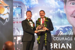 Two men in suits with leis presenting courage award at corporate gala, event photography Dallas, Texas