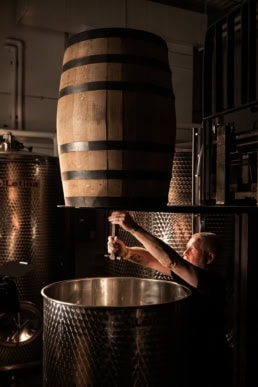 Blackland Distillery worker pouring from oak barrel into steel tank, industrial photography Fort Worth, Texas