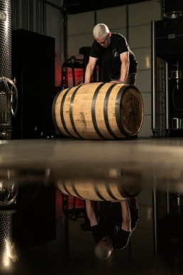 Blackland Distillery worker rolling oak barrel across polished floor, commercial photography Fort Worth, Texas