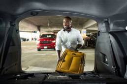 Traveler loading yellow suitcase into car trunk at DFW Airport parking garage, commercial photography Dallas, Texas