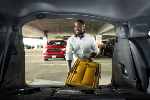 Traveler loading yellow suitcase into car trunk at DFW Airport parking garage, commercial photography Dallas, Texas