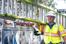 Spectrum technician carrying ladder next to service truck, industrial photography Dallas, Texas