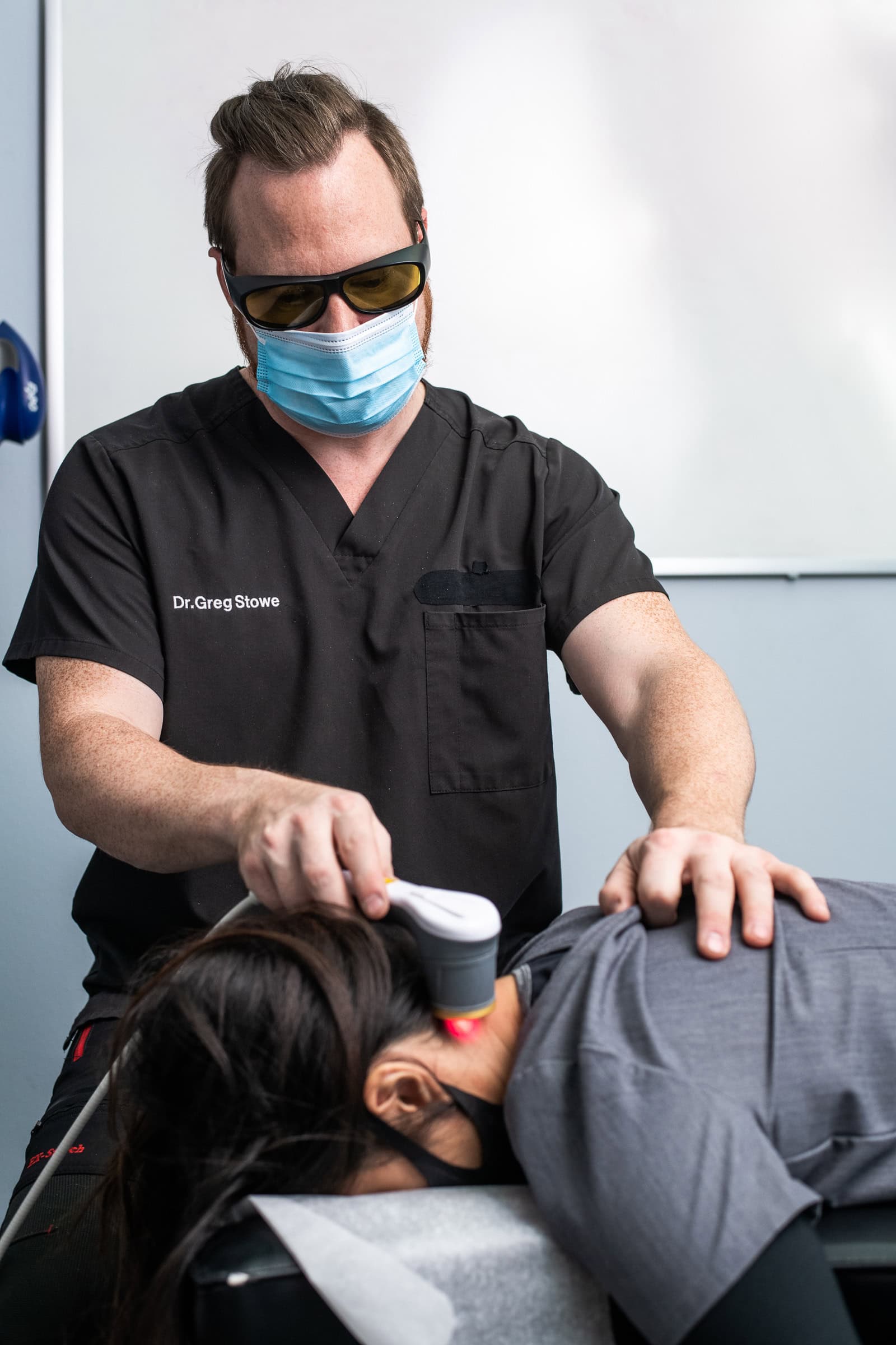 Physician performing laser therapy on a patient in the treatment room, commercial medical photography in Dallas, Texas by David Loi Studios