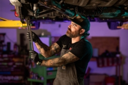 Tattooed mechanic using torque wrench under lifted vehicle, automotive photography Dallas, Texas