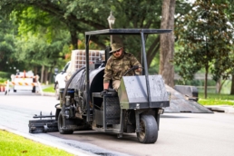 TAS Concrete sealcoat machine operator applying asphalt sealer, industrial photography Houston, Texas