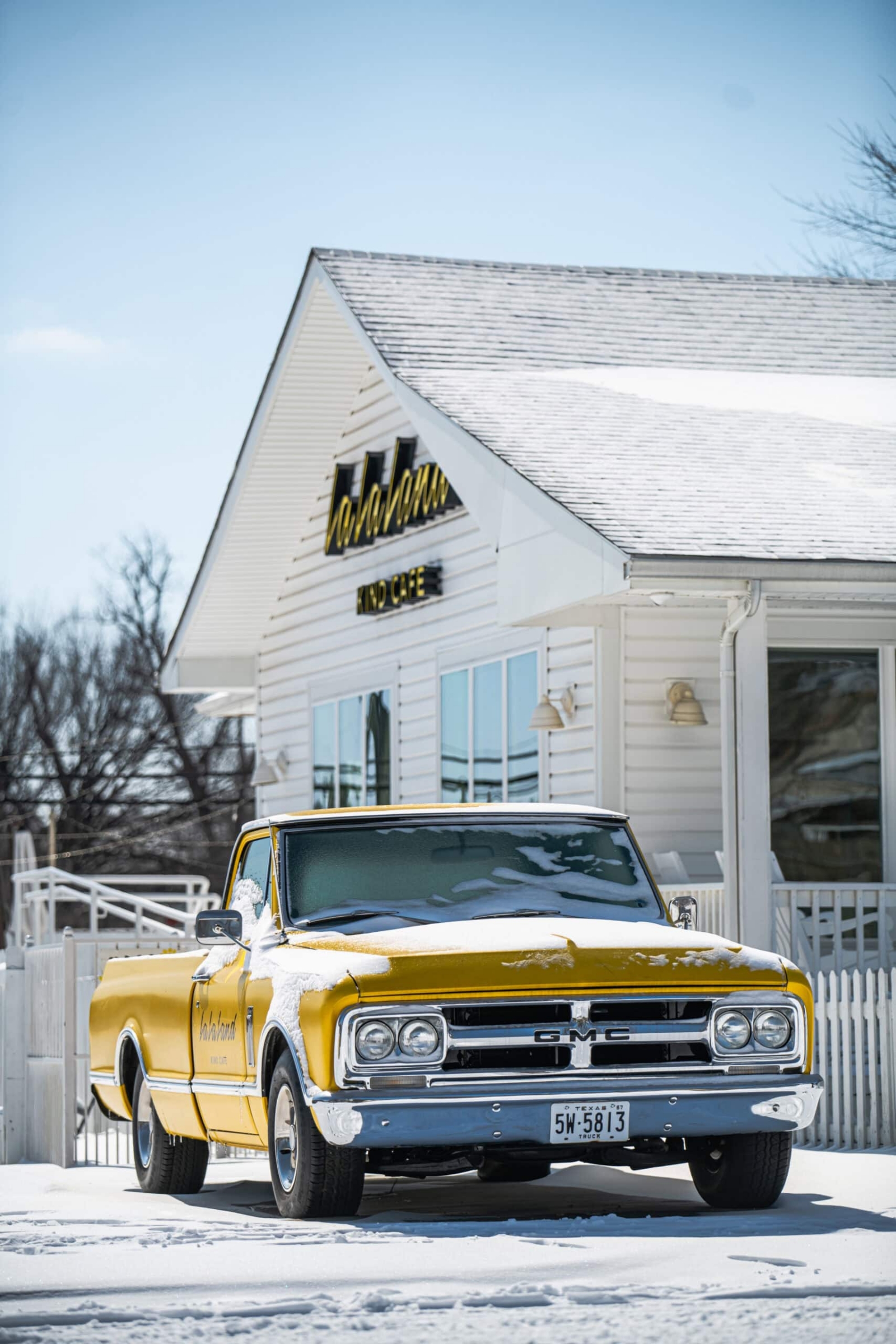 Vintage yellow GMC pickup truck covered in snow outside La La Land Kind Cafe, commercial photography Dallas, Texas